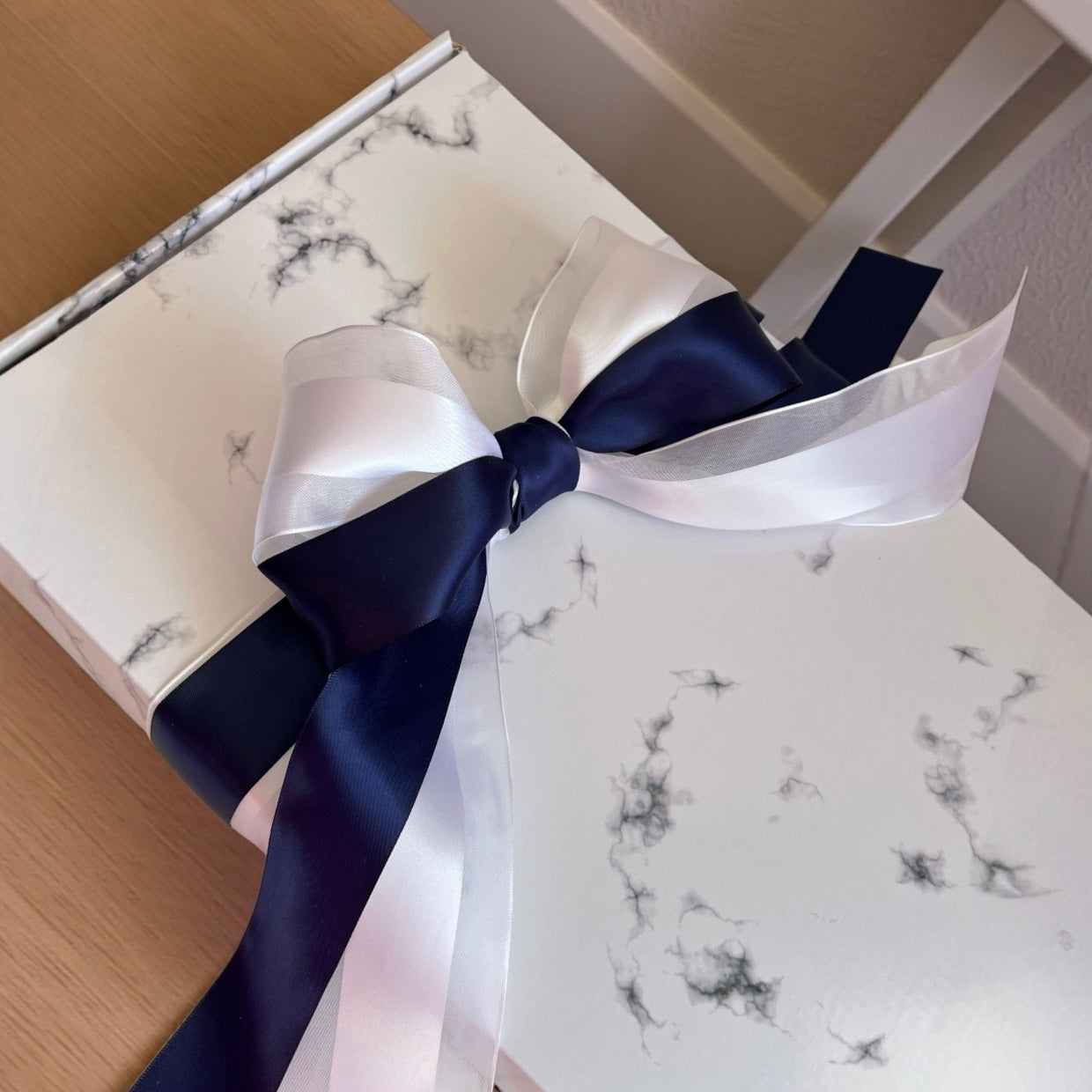Gift box with a large white and navy blue bow on a marble-patterned surface.