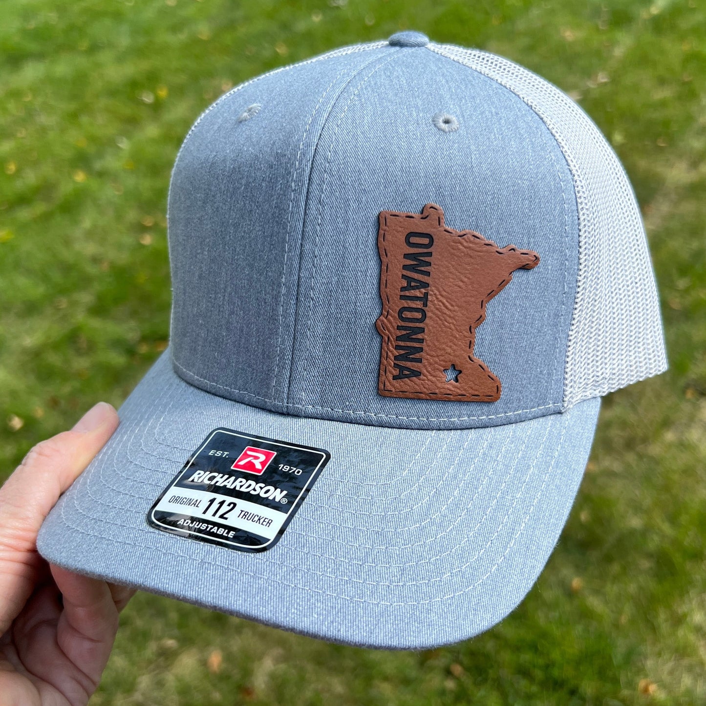 Gray Richardson 112 trucker hat with leather like patch in the shape of Minnesota and the words Owatonna.