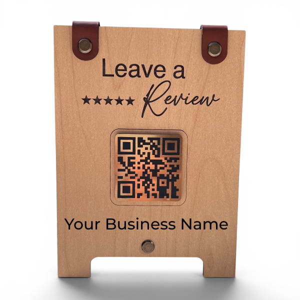 A personalized wooden business review stand with a natural wood finish, black engraved text, a central QR code window, and two brown leather loops at the top, shown on a white background.