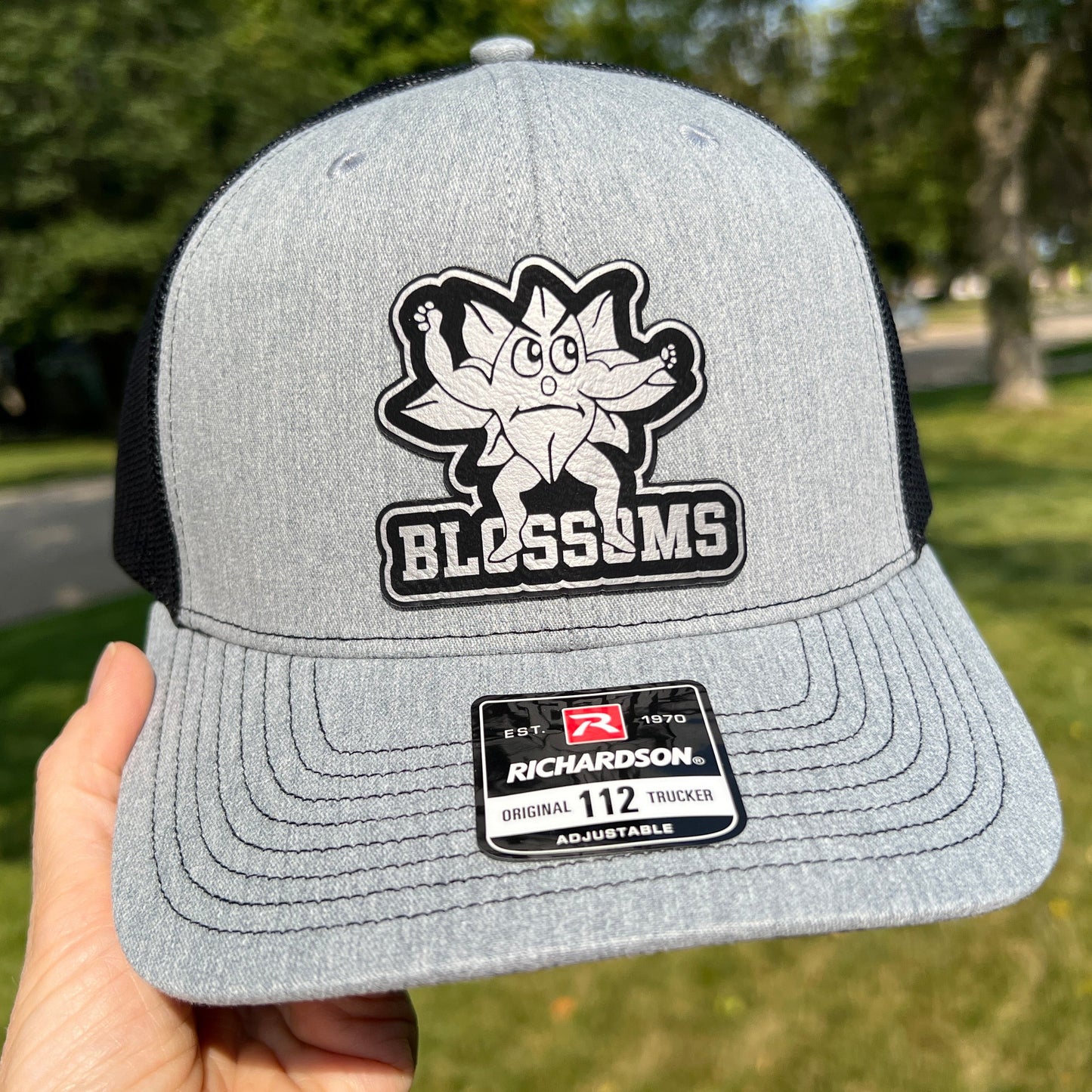 Grey and Black Richardson 112 trucker hat with a black and silver blossoms patch on the front.