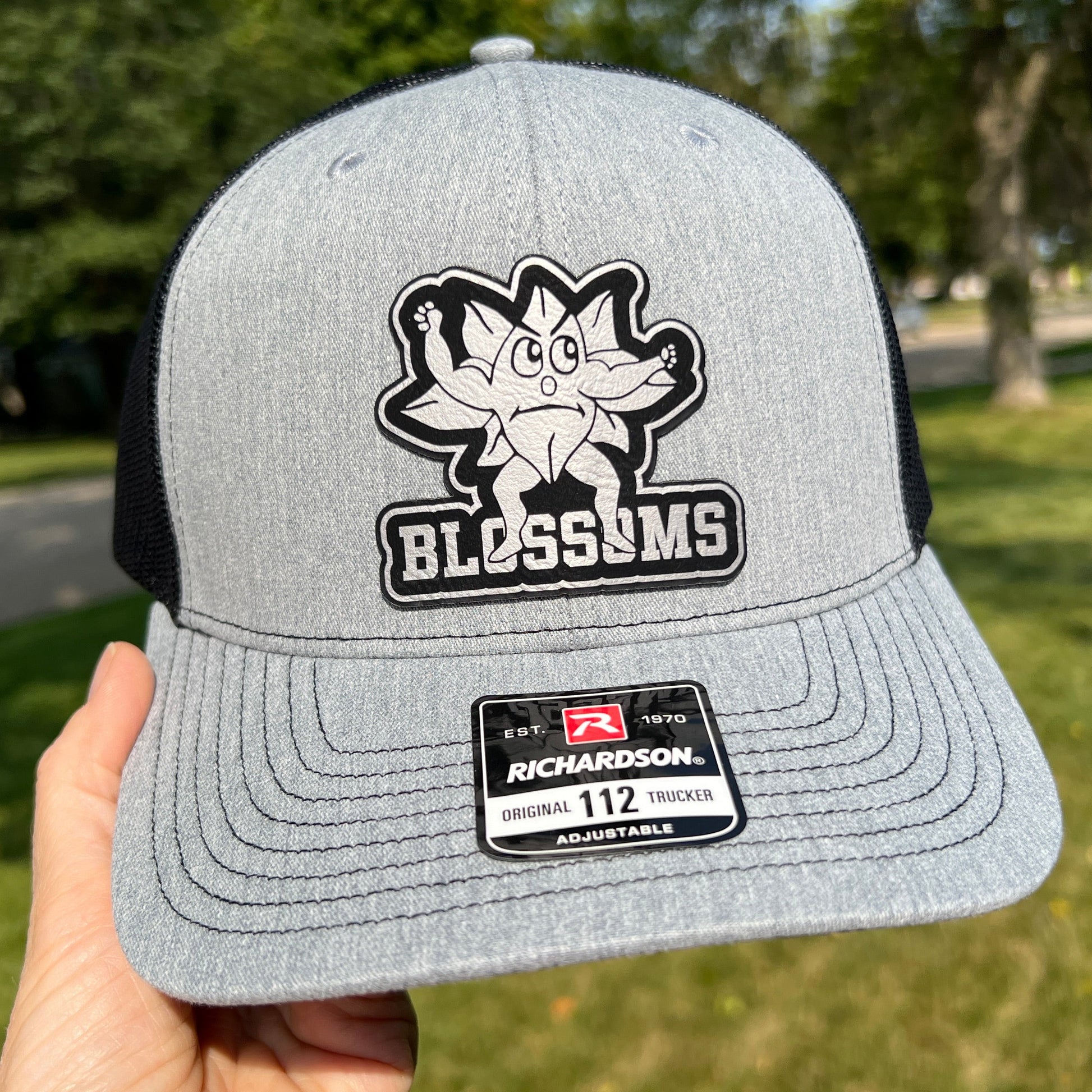 Grey and Black Richardson 112 trucker hat with a black and silver blossoms patch on the front.