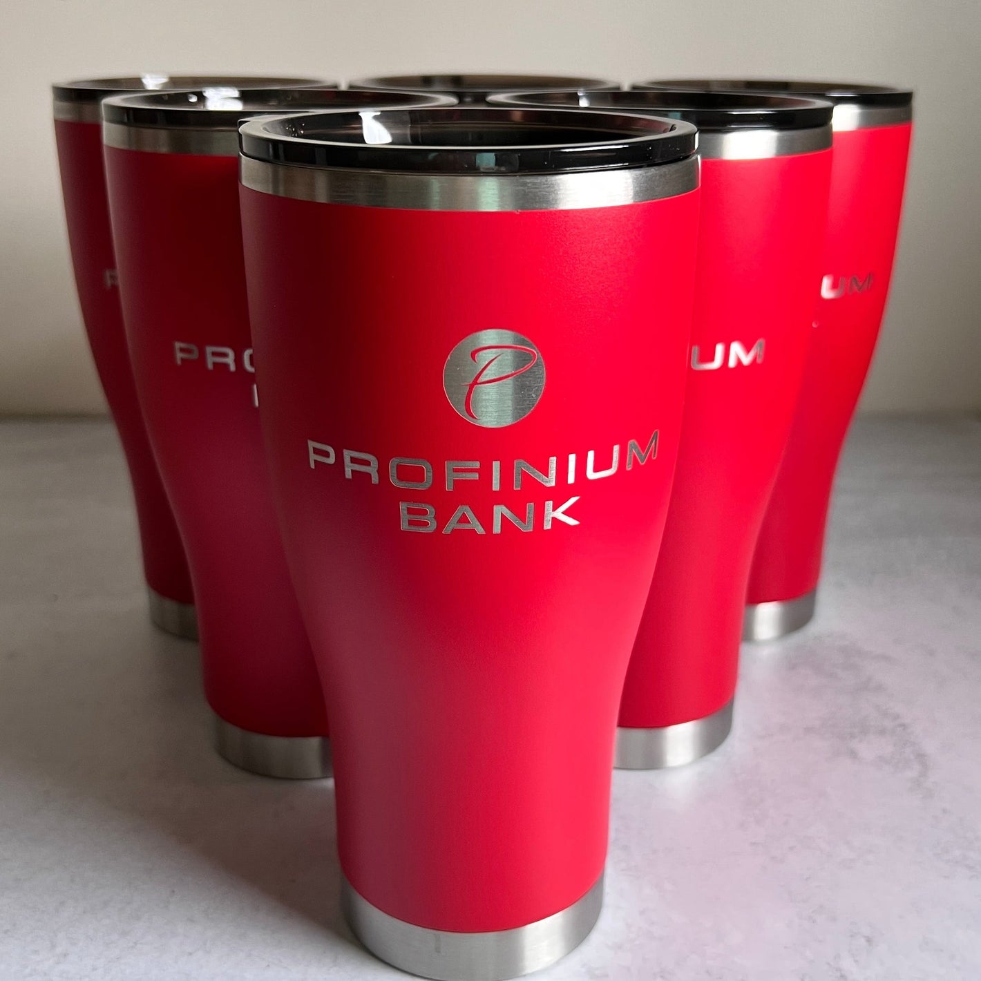Red tumblers with a silver logo and text on a light surface