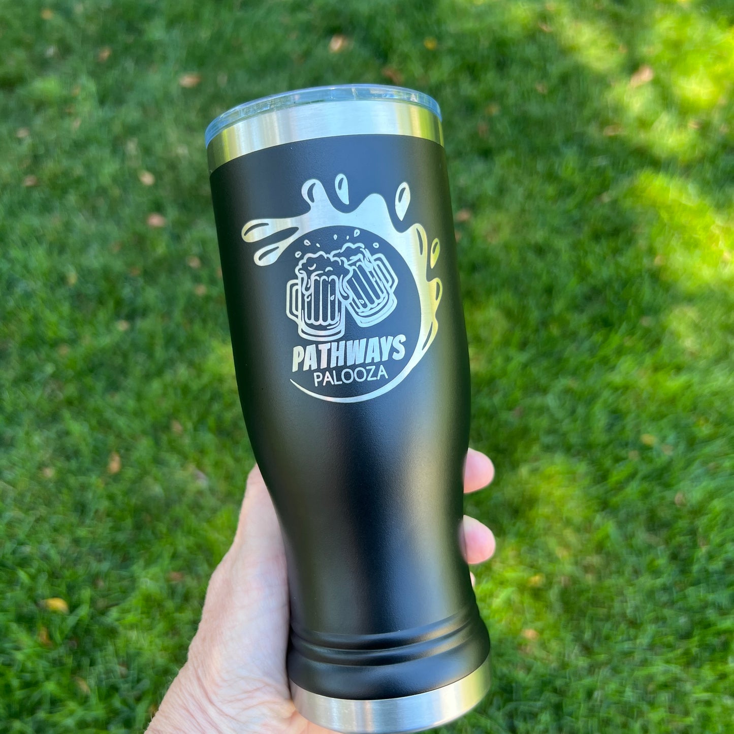 Black tumbler with 'Pathways Palooza' logo held in front of green grass