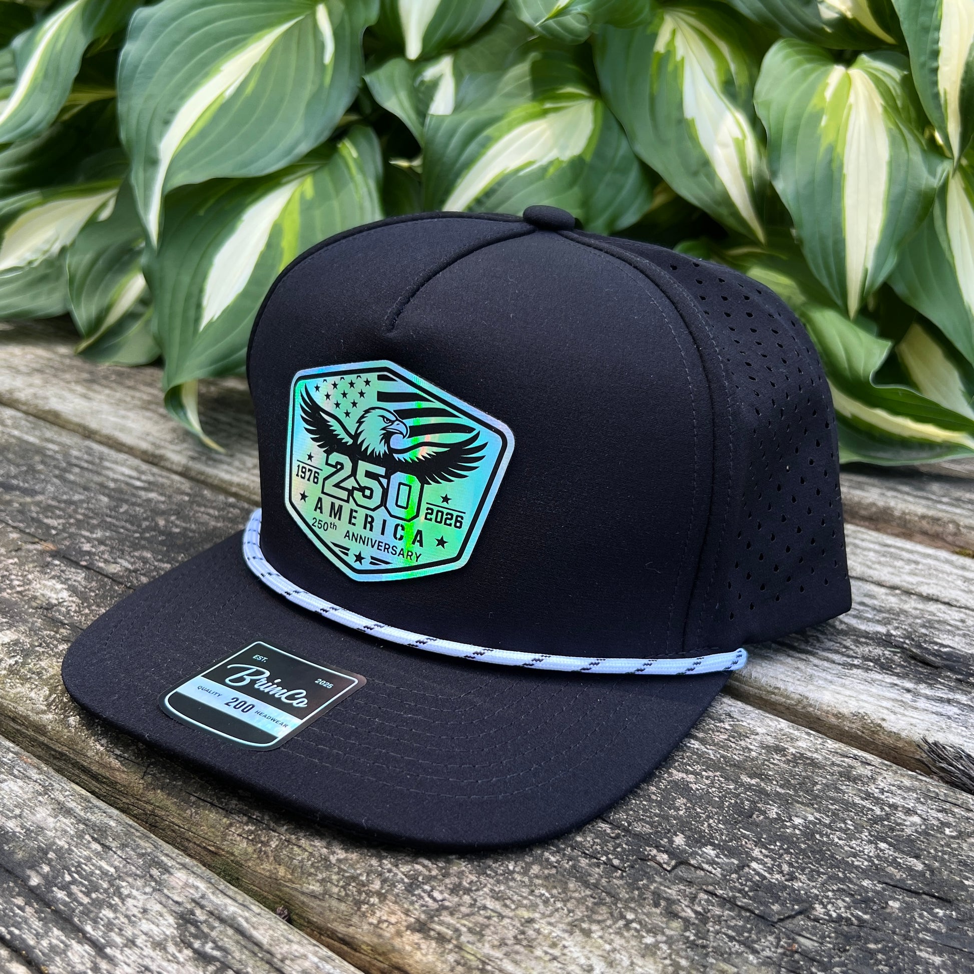 Black cap with a green and white emblem on a wooden surface with green leaves in the background