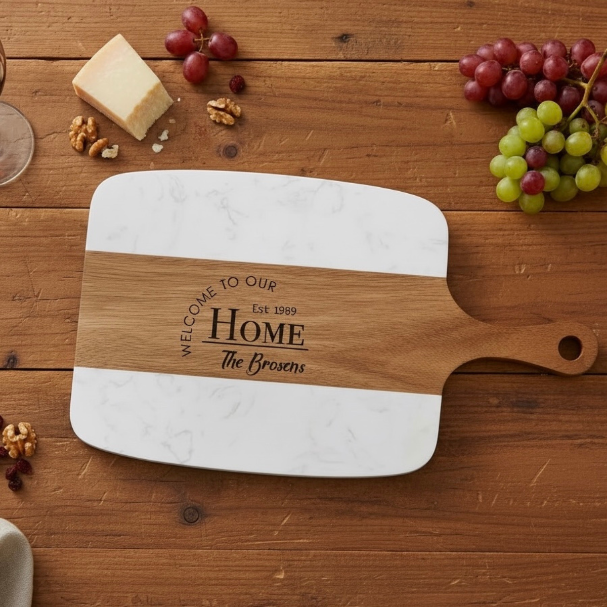 Personalized cutting board with marble finish and wooden handle on a wooden table with grapes and cheese.