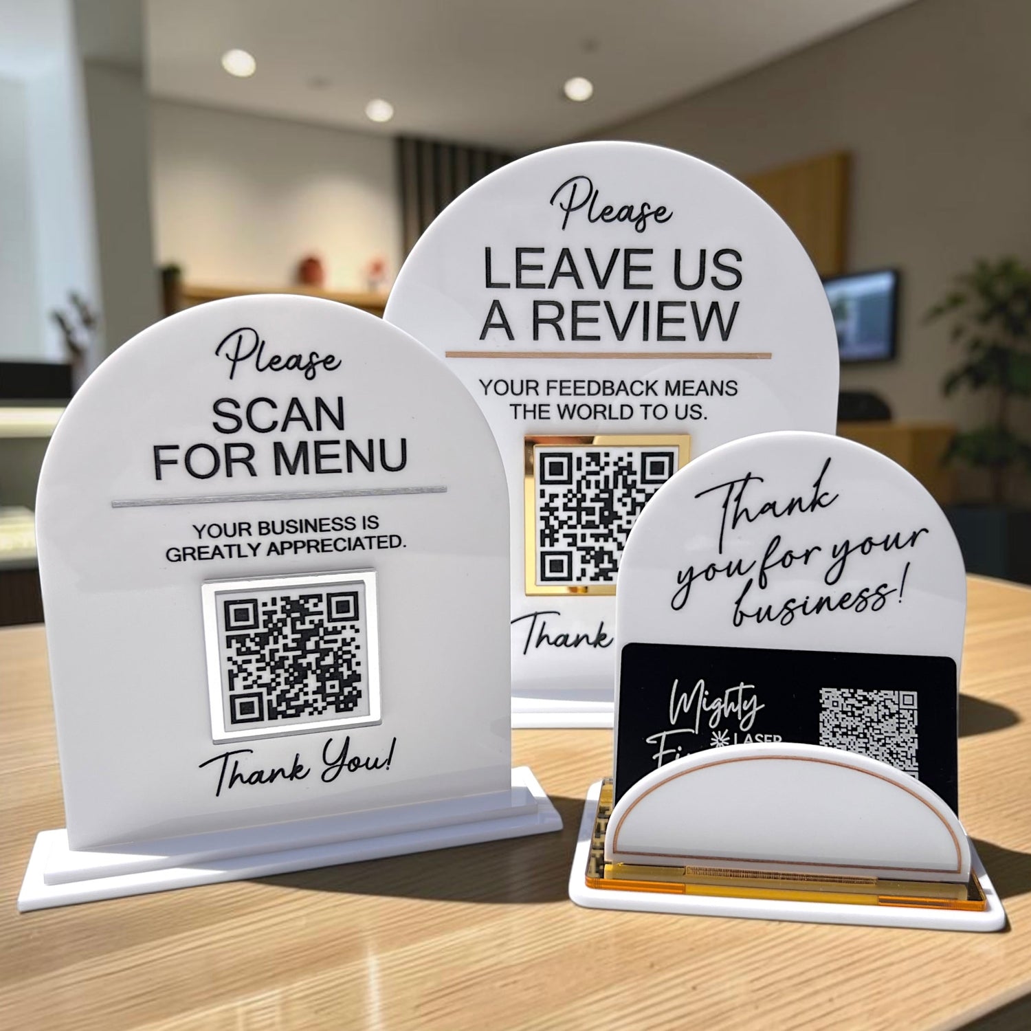 2 White displays with QR codes with black wording, leave us a review, scan for menu. 1 white business card holder with black and gold accents, thank you for your business.