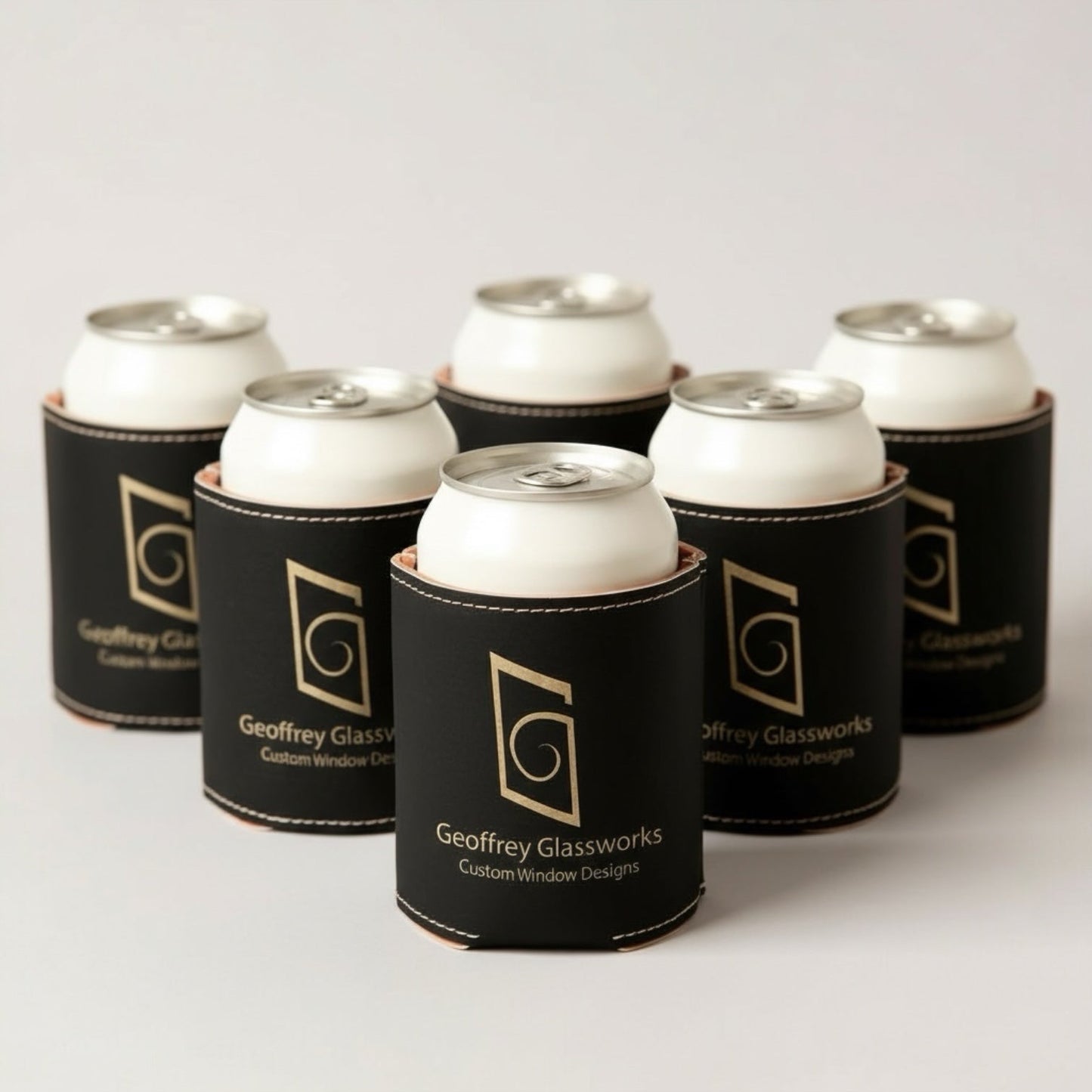 Six black can coolers with gold engraved Geoffrey Glassworks logo on a light gray background