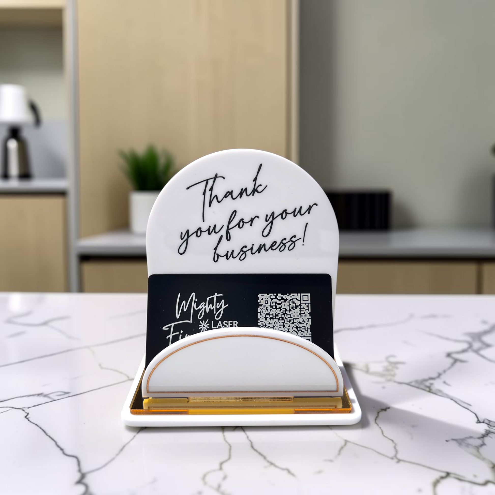 A white acrylic business card holder and sign set on a white marble countertop. The set includes a white semi-circular sign with black script reading 'Thank you for your business!' and a card slot holding with gold metallic edges.