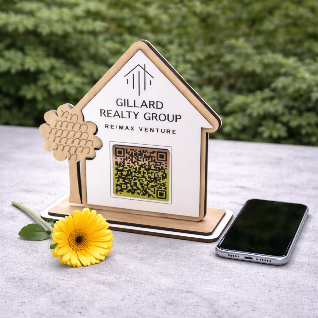 Gillard Realty Group sign with QR code on a stand next to a yellow flower and smartphone.